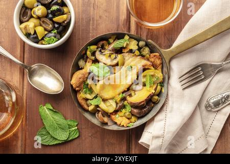 Un rustico di funghi e olive saute, girato dalla parte superiore in una ghisa pan con la menta e il vino al buio su un sfondo di legno Foto Stock