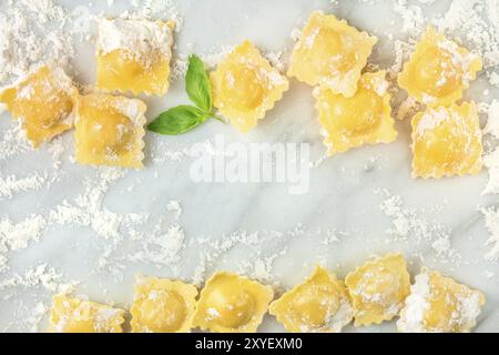 Ravioli con la farina e le foglie di basilico, formando una cornice, ripresa dall'alto su un marmo bianco sfondo con copia spazio, un modello di progettazione per una ricetta Foto Stock