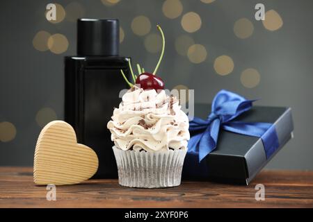 Buona festa del papà. Cupcake, confezione regalo, cuore in legno e profumo sul tavolo contro luci sfocate Foto Stock