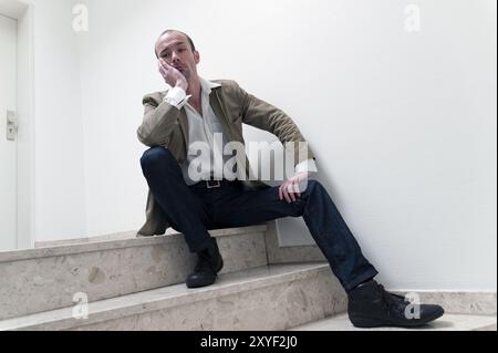 Il giovane uomo si siede da solo sui gradini del corridoio Foto Stock