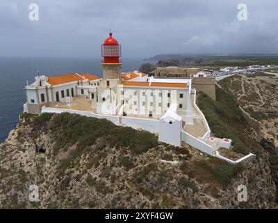 Un faro rosso su una scogliera rocciosa, circondato da edifici bianchi, con una vista spettacolare dell'oceano, vista aerea, faro, Cabo de Sao Vicente, Cap Foto Stock