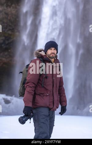 Ritratto di un fotografo in inverno alla cascata Seljalandsfoss con neve in Islanda Foto Stock