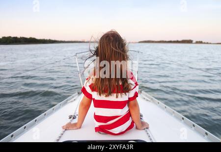 Carino bambina godendo di cavalcare su yacht al tramonto Foto Stock