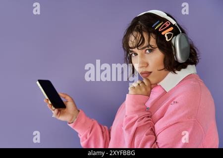 Una donna, vestita di rosa vibrante, regge con cura il suo telefono su uno sfondo viola brillante. Foto Stock