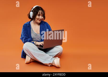 Una donna con le cuffie si siede sul pavimento e utilizza un notebook. Foto Stock