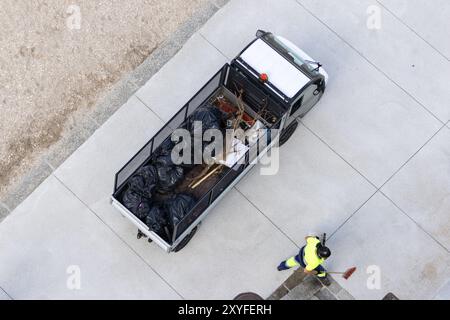 Vista aerea di un veicolo elettrico carico di sacchetti per la spazzatura e di un pulitore stradale che lavora per raccogliere rifiuti in una zona balneare della città Foto Stock