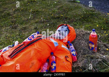 DJUPIVOGUR, ISLANDA, 21 GIUGNO: Manichino maschile giace sull'erba ricoperto di bottiglie di succo d'arancia il 21 giugno 2013 a Djupivogur, Islanda, Europa Foto Stock