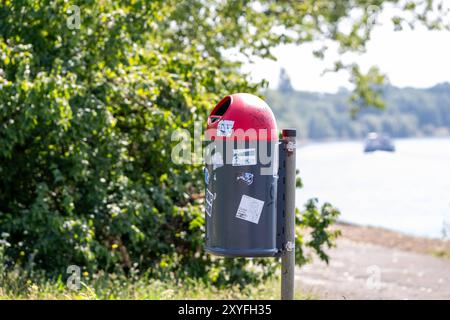 Mülleimer am Rheinufer mit Graffiti und Aufklebern , Deutschland, 29.08.2024, Ein Mülleimer am Rheinufer, beklebt mit Aufklebern und Graffiti, steht vor einer Grünen, unscharfen Naturkulisse. DAS Bild zeigt den Kontrast zwischen städtischer Infrastruktur und Natur. *** Trash CAN sulle rive del Reno con graffiti e adesivi , Germania, 29 08 2024, Un cestino sulle rive del Reno, ricoperto di adesivi e graffiti, si erge di fronte a uno sfondo naturale verde e sfocato l'immagine mostra il contrasto tra infrastrutture urbane e natura Foto Stock