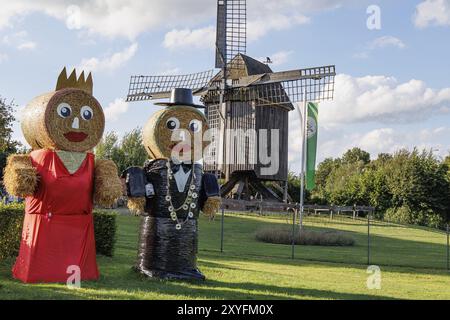 Due grandi bambole di paglia di fronte a uno storico mulino a vento su un prato verde, Weseke, muensterland, germania Foto Stock