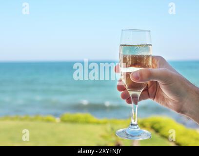 Bicchiere di champagne in mano sulla spiaggia Foto Stock