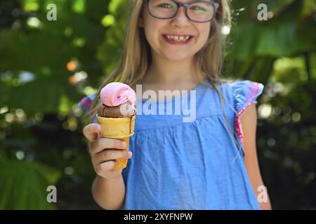 Carino Bambina con espressione divertente tenendo cono gelato al di fuori contro natura brillante background. Close up Foto Stock