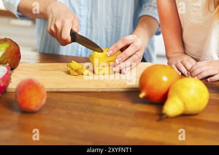 Bellissima bambina con la madre in cucina preparare una macedonia di frutta fresca. Close up Foto Stock