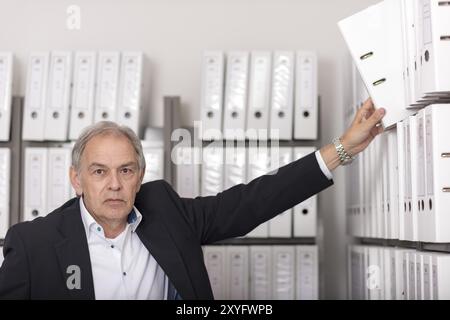 Un uomo anziano in camicia bianca mette una cartella di documenti su uno scaffale Foto Stock