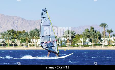 Windsurfer cavalca sulle onde del Mar Rosso sullo sfondo della spiaggia con palme e alte montagne in Egitto Dahab Foto Stock