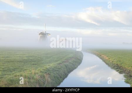 Mulino a vento nella nebbia mattutina sul fiume, Olanda Foto Stock