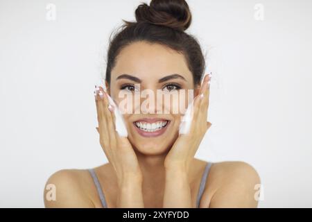 Giovane e bella bruna donna caucasica lavando il suo volto con schiuma Foto Stock