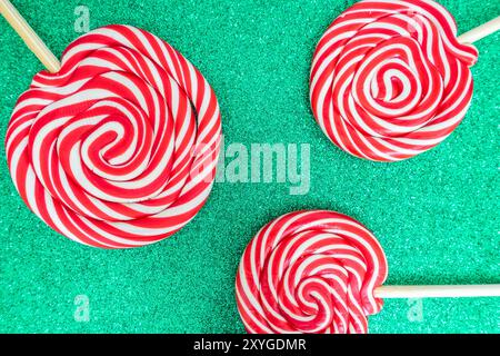 Tre lollypop natalizi su uno sfondo verde e scintillante. Sfondo per Natale con spazio di copia per il testo. Foto Stock