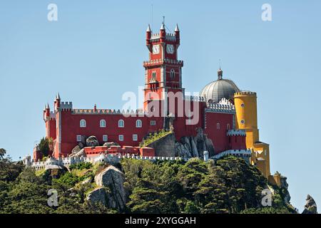 SINTRA, Portogallo - Palácio da pena, arroccato sulla cima di una collina dei Monti Sintra, visto da lontano. La colorata ed eclettica architettura di questo castello romanticista del XIX secolo si distingue drammaticamente contro il lussureggiante paesaggio verde, incarnando il fascino fiabesco per cui Sintra è famosa. Foto Stock