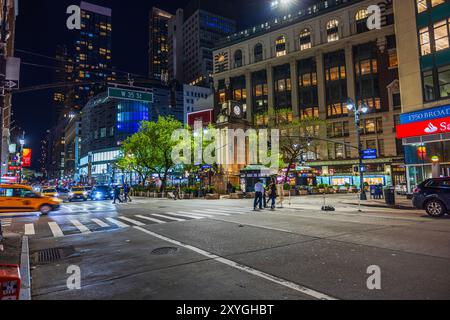 Vista notturna della strada della città di New York con edifici, alberi e auto sotto i semafori. New York. STATI UNITI. Foto Stock