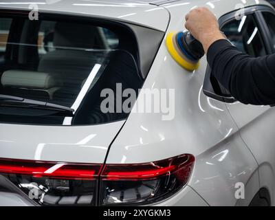 Processo di lucidatura della superficie bianca della carrozzeria della vettura con una lucidatrice orbitale. Foto Stock