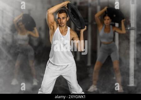 Primo piano di un atletico sportivo in piedi con un piatto di barbell in mano nella sala fitness Foto Stock