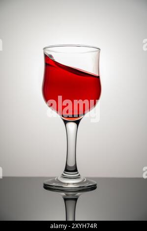 Vino rosso che spruzza nel bicchiere su sfondo bianco. Copia spazio. Foto Stock