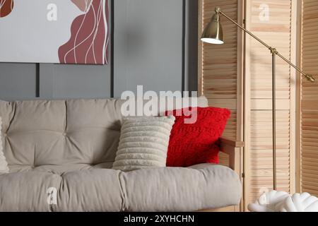 Schermo pieghevole in legno, comodo divano con cuscini e lampada in camera Foto Stock