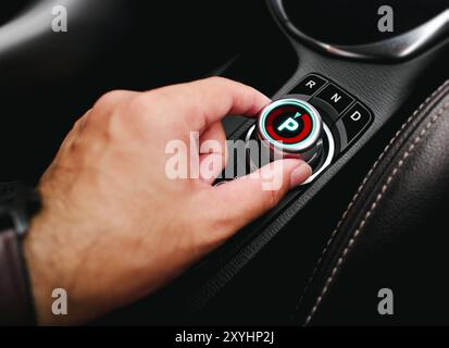 Mano del conducente che gira un selettore marce rotativo sul cruscotto di un'auto EV o di un veicolo elettrico , P posizione cambio parcheggio , tecnologia auto elettrica con Foto Stock