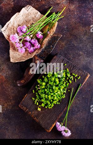 Erba cipollina verde o allio in fiore con fiori viola viola e steli verdi su un tavolo di legno, erba cipollina è un'erba commestibile per l'uso in cucina. Foto Stock