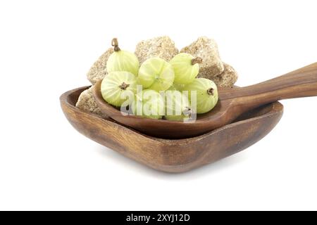 Uva spina verde matura in un cucchiaio di legno accanto ai cubetti di zucchero di canna in un recipiente di legno, per conservare gli alimenti Foto Stock