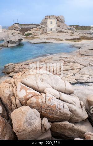 Scogliera di Punta Tegge, una spiaggia di granito con scogli erosi in primo piano e una torre storica sullo sfondo sull'isola di la Maddalena, a Sardin Foto Stock