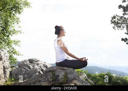 Attraente giovane donna facendo un po' di yoga pone sulla sommità della roccia alta in montagna giornata soleggiata cielo blu con nuvole Foto Stock