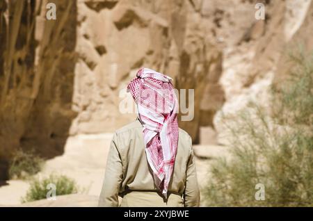 Beduino in bianco va nel canyon nel deserto tra le rocce Foto Stock