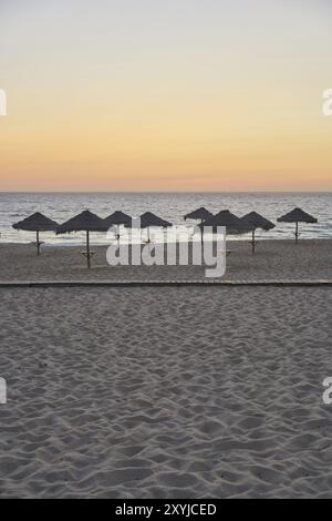 Spiaggia vuota al tramonto a Comporta, Portogallo con ombrelloni estivi di paglia Foto Stock