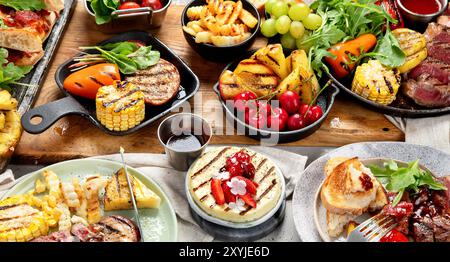 Tavolo con piatti alla griglia. Pizza, mais, pomodori, peperoni, carne cotta. Barbecue. Foto Stock