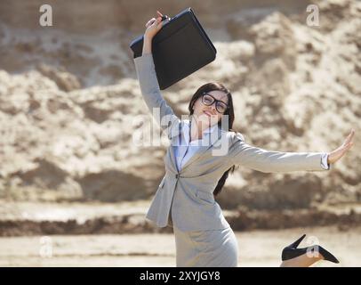 Felice donna d'affari che salta in aria in un deserto Foto Stock