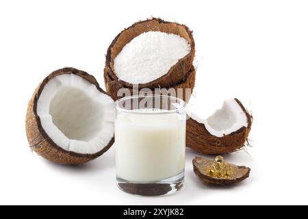 Prodotti al cocco. Latte di cocco in un bicchiere con gusci di cocco, olio in capsule e fiocchi isolati su bianco. Messa a fuoco selettiva Foto Stock