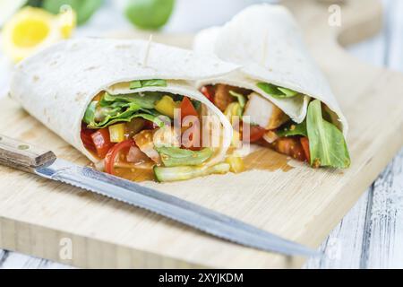 Wrap di pollo (primo piano dettagliato, messa a fuoco selettiva) su sfondo in legno Foto Stock