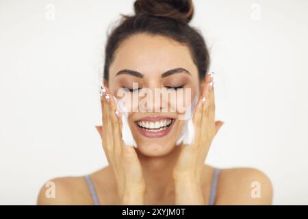 Giovane e bella bruna donna caucasica lavando il suo volto con schiuma Foto Stock