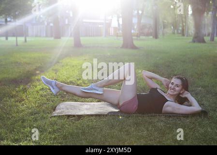 Donna che si allunga in un esercizio all'aperto sorridente felice facendo stretching dopo la corsa. Splendido modello sportivo sorridente all'aperto al tramonto d'estate Foto Stock