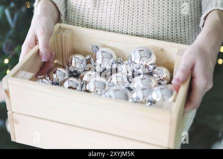 Donna contiene una scatola con un sacco di Natale decorazioni argento vicino all'albero di Natale. Vacanze di Natale concetto. Close up Foto Stock