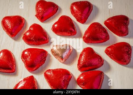 Un cuore chocoalte in carta da imballaggio rosa, circondato da molti cuori in carta da imballaggio rossa Foto Stock