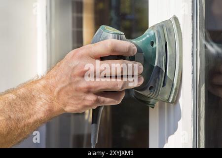 La mano del pittore di levigatura sul telaio di una finestra con levigatrice elettrica Foto Stock