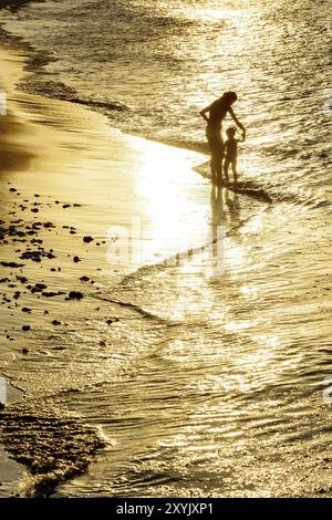 Madre e figlia giocano insieme in acqua durante il tramonto Foto Stock