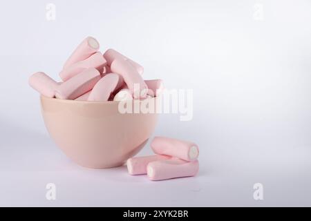 Una ciotola rosa traboccante di marshmallow è presente al centro di questa immagine con cornice orizzontale, con una piccola pila di marshmallow sulla sinistra. Foto Stock