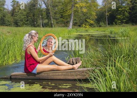 Bionda e giovane donna olandese si siede con specchio ad acqua in natura Foto Stock