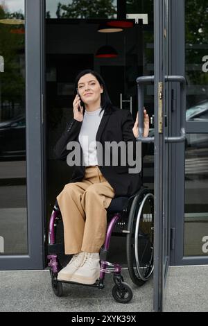 Una donna in sedia a rotelle sta entrando in un edificio mentre parla al telefono. Foto Stock