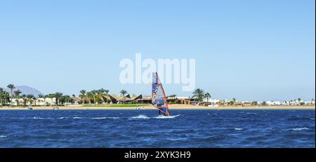 Windsurfer cavalca in mare sullo sfondo della spiaggia con palme e alte montagne rocciose in Egitto Dahab Foto Stock