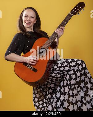 Bruna chitarrista donna in abito lungo su sfondo giallo Foto Stock