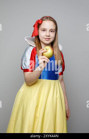 Bella bambina che indossa il costume Biancaneve tenendo in mano una mela su sfondo bianco, ritratto Foto Stock